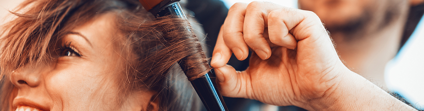 Escena de peluquería de una chica a la que le están haciendo rizos con la plancha de pelo